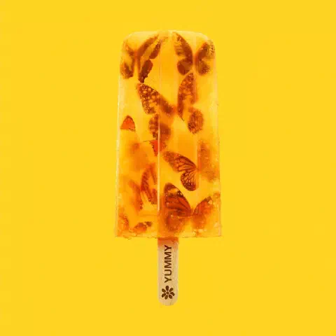 A square album cover for Yummy by James. The cover art shows the yellow version of the album with a yellow ice lolly on a yellow background containing orange butterflies. The name 'Yummy' is printed on the wooden ice lolly stick.