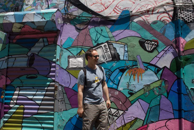 A photo of a person standing in front of a colourful graffiti covered wall.