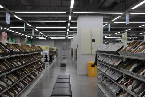 A photo taken inside a shoe store. There are rows of shoes neatly arranged on shelves eaither side of an isle. Down the centre of the aisle is a row of cushioned benches.