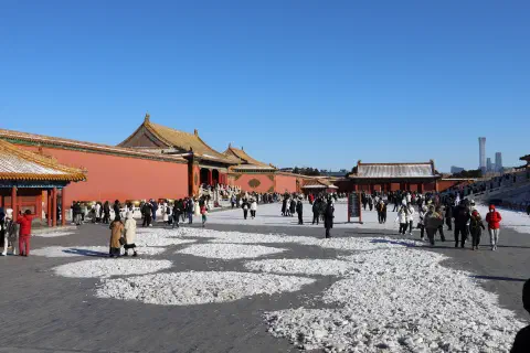 A snow covered courtyard in the Forbidden City, Beijing. Warmly dressed people are standing around on the snow.