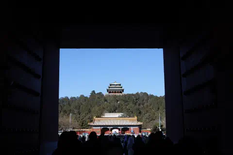 A photo taken through the gates of the Forbidden City looking up at Jingshan Temple in the distance. The image is exposed in such a way that the walls of the gate provide a black frame to the main image of the temple.