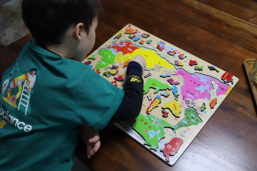 A child completes a jigsaw puzzel of a map of hte world.