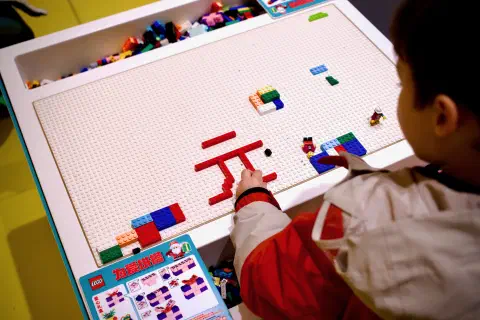 A child uses LEGO bricks to make Chinese characters on a table.