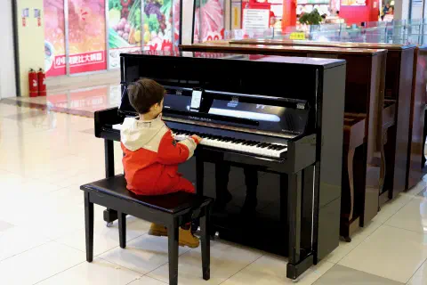 A young child sits at a piano in a shopping mall.