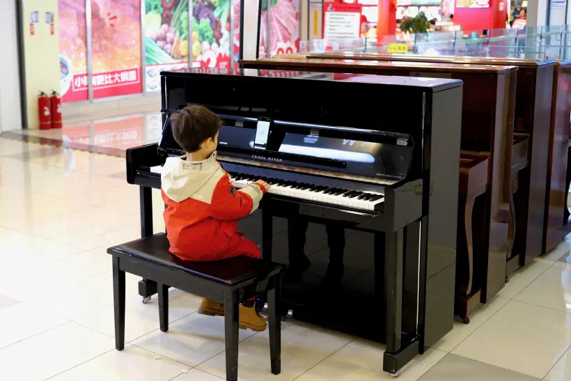 A young child sits at a piano in a shopping mall.