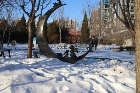 A sculpture of rabbits sittting inside a crescent moon sits on the snow covered gound in a Beijing park.