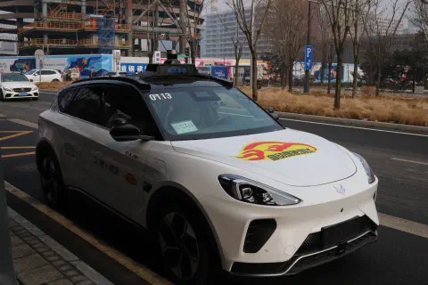 A photo of a white driveless taxi parked up at the side of the road in Beijing.