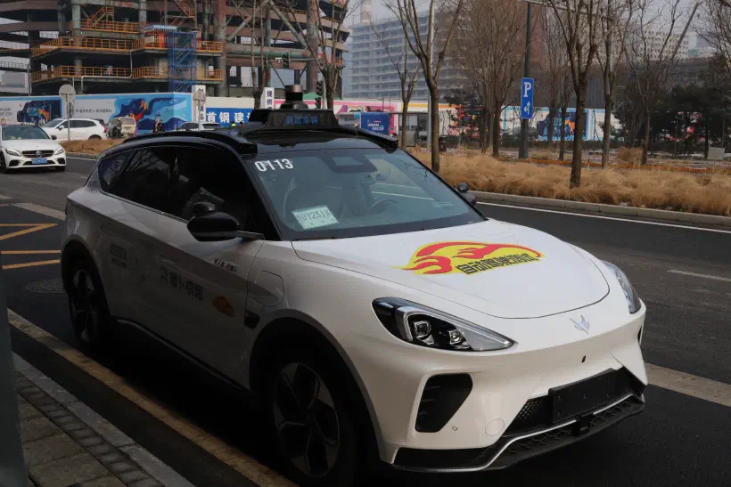 A photo of a white driveless taxi parked up at the side of the road in Beijing.