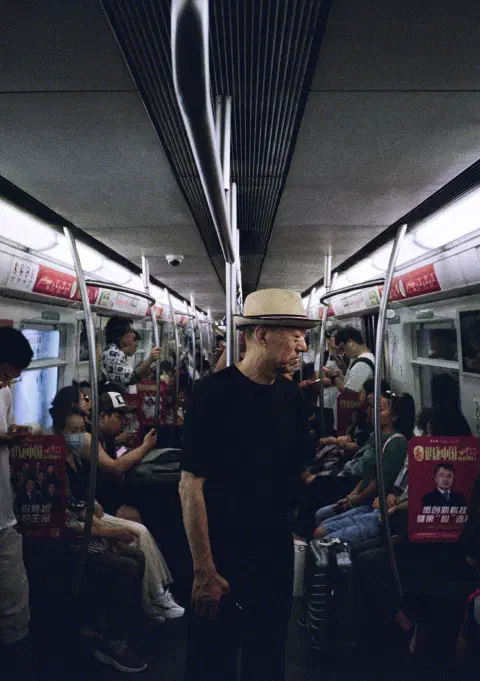 A photograph taken inside a subway train in Beijing. In the centre of the carriage stands a man looking off to the right of the image. We can't see what he is looking at. He appears to be smiling.