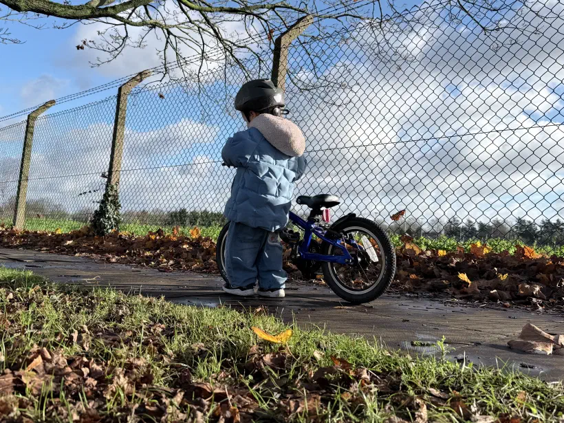 A young boy standing next to his small bike looking away from the camera