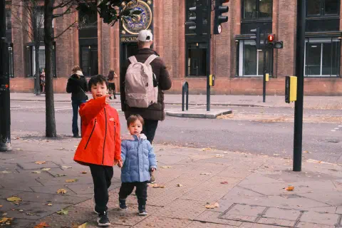 Two boys walk on the streets of London, the older points to something behind the camera