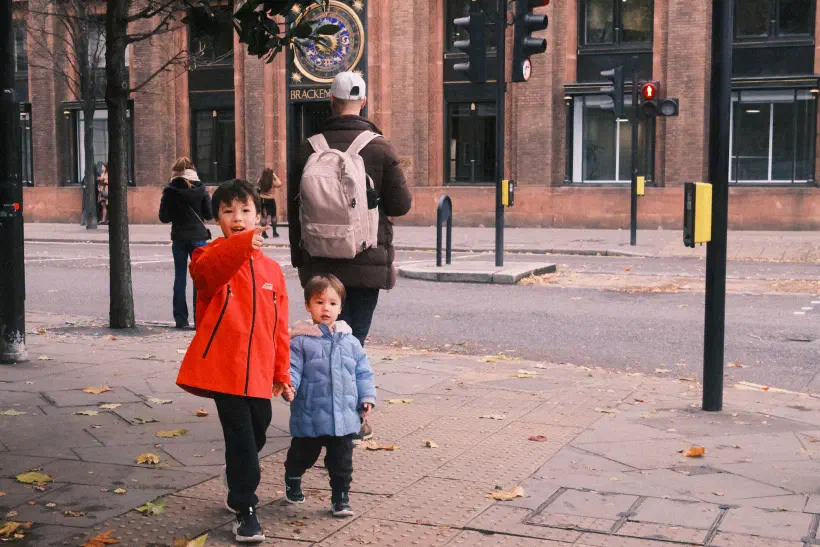 Two boys walk on the streets of London, the older points to something behind the camera