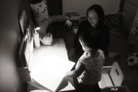 a black and white photo of a young boy and his mother looking at a book