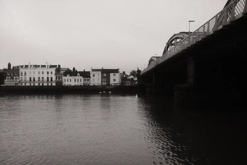 a black and white photo looking over the River Thames towards Barnes Bridge station