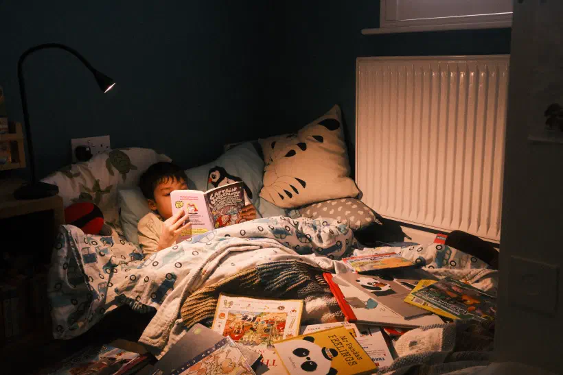 a boy lies in a makeshift bed surrounded by books