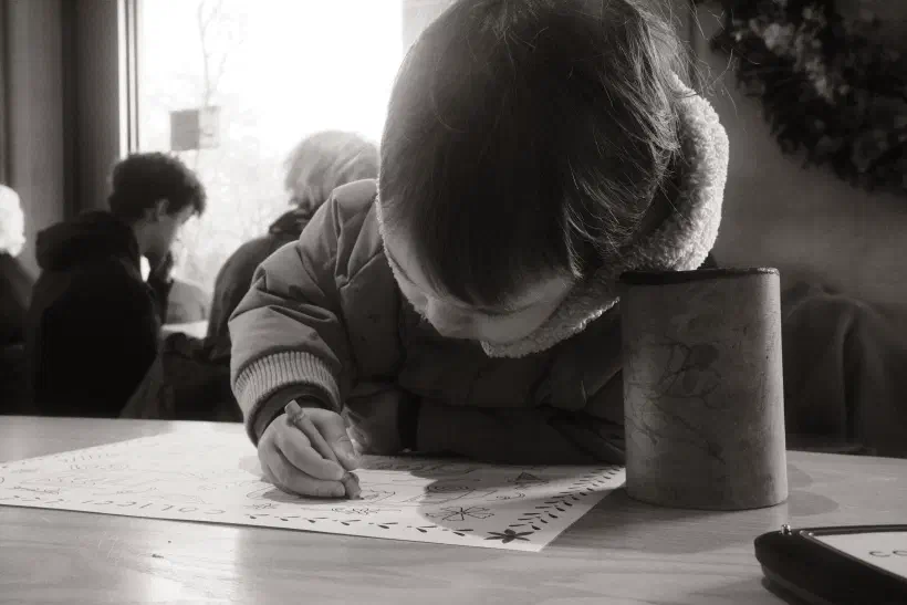 a young boy hunched over a piece of paper, a blunt crayon in one hand