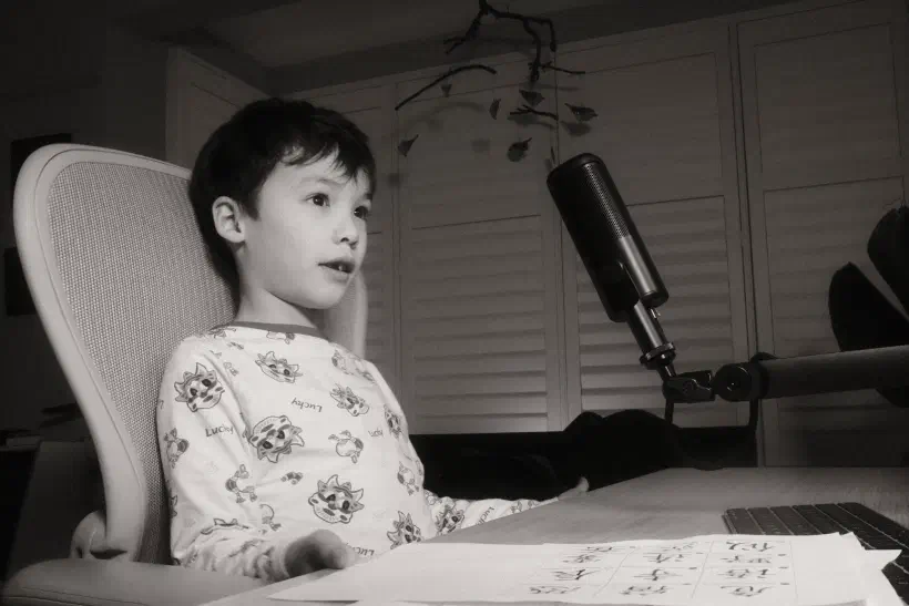 a black and white photo of a boy sitting at a desk in front of a microphone