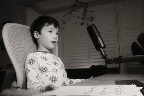 a black and white photo of a boy sitting at a desk in front of a microphone