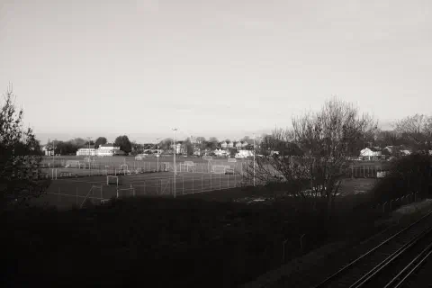 a black and white photo of playing fields, a railway track in the foreground