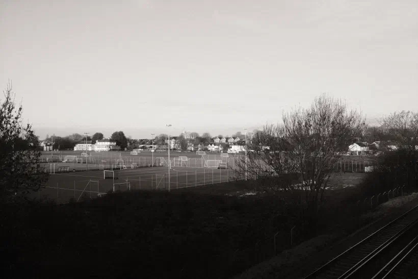 a black and white photo of playing fields, a railway track in the foreground