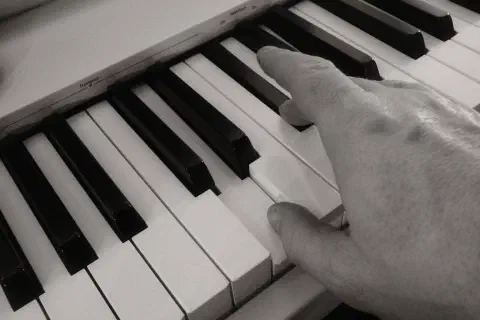 A black and white photo of a hand on a keyboard, the thumb playing the note D.