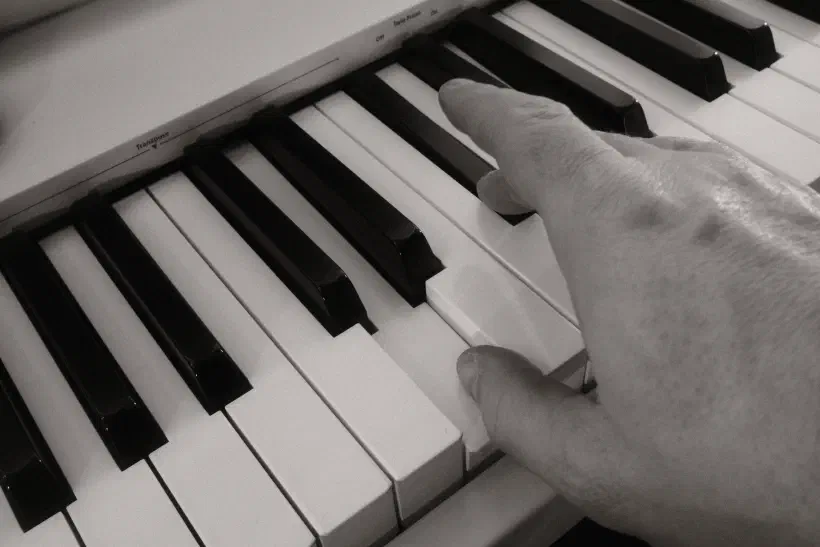 A black and white photo of a hand on a keyboard, the thumb playing the note D.