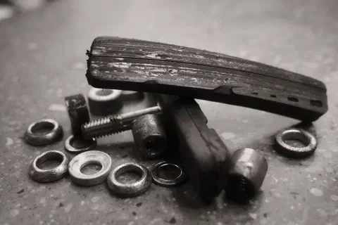 A black and white photo showing a collection of bike parts. Heavily worn brake pads and their mounting rinngs lay i a small pile on a work surface.