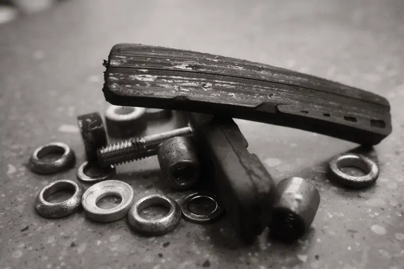 A black and white photo showing a collection of bike parts. Heavily worn brake pads and their mounting rinngs lay i a small pile on a work surface.
