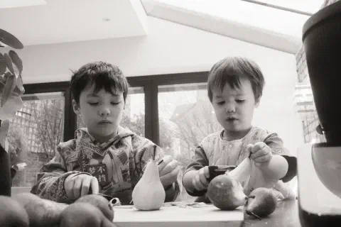 A black and white photo showing two boys peeling pears.