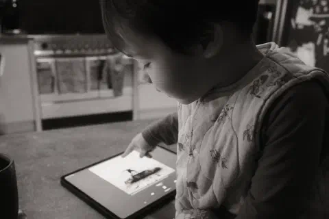 A black and white photo of a young child pointing at an iPad. On the iPad is the cover of 1975's Being Funny in a Foreign Language.
