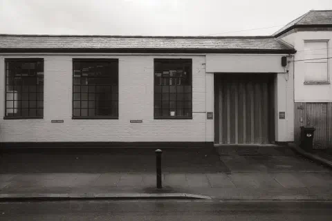 Black and white photo of a small warehouse style building. The doors are closed.