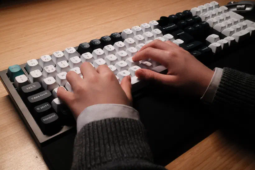 The hands of a child rest on a computer keyboard