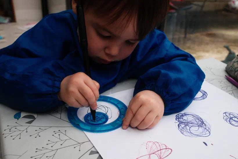 a photo of a child making geometric patterns by using concentric gears to rotate a pen across paper