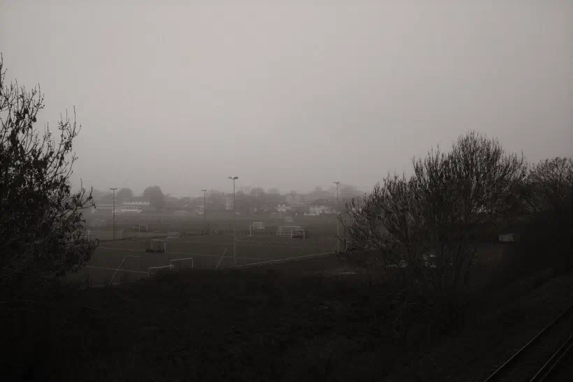 A black and white photo looking out over playing fields on a foggy morning.