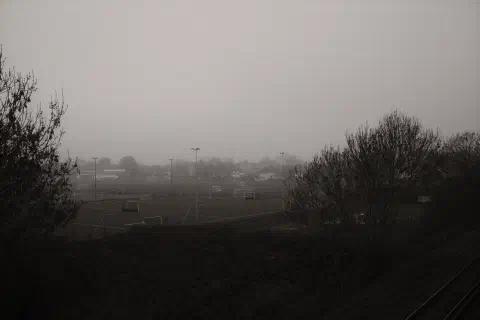 A black and white photo looking out over playing fields on a foggy morning.