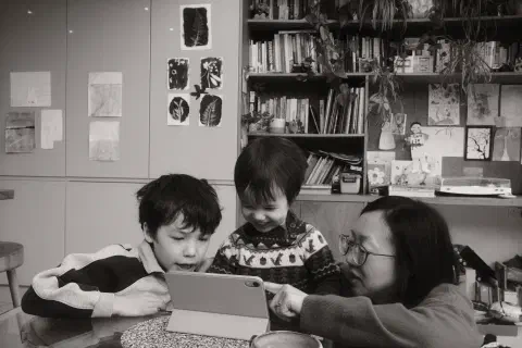 Two boys and their mother huddle around an iPad. The youngest is in the middle smiling. The mother points to something on screen.