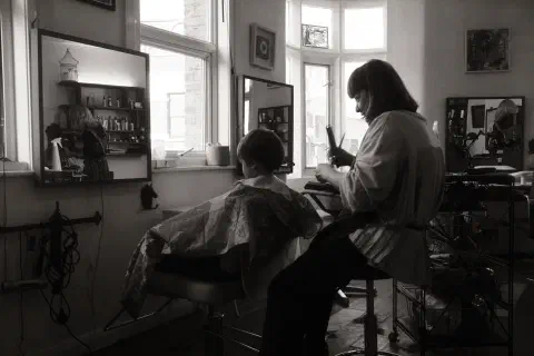 A black and white photo of a young boy sat having his haircut
