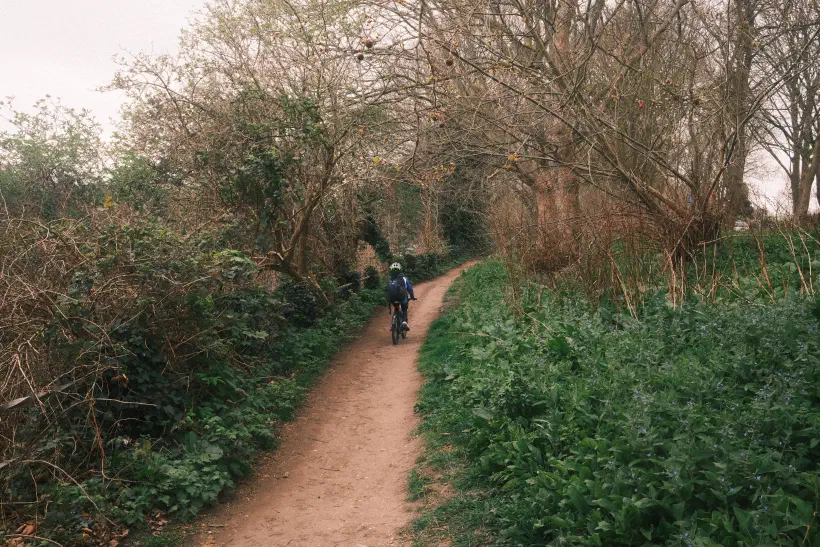 a boy cycles off along a dirt track, bushes either side of the trail