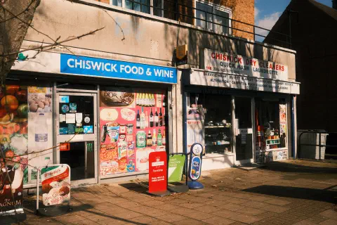 a photo of two adjacent shops, Chiswick Food & Wine and Chiswick Dry Cleaners, the front of each covered with posters and advertisements
