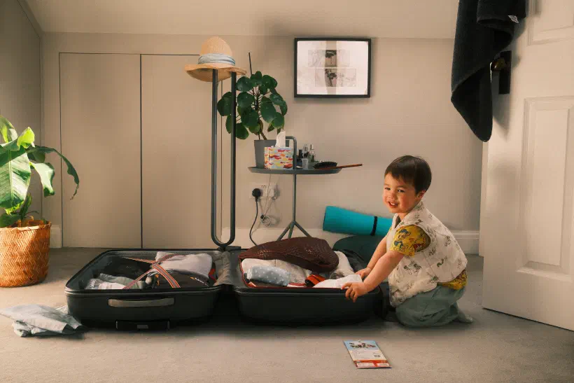 a young boy kneels beside a packed suitcase