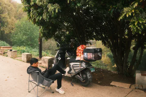 a moped rider pulls up to rest, birdcage on the back of his bike