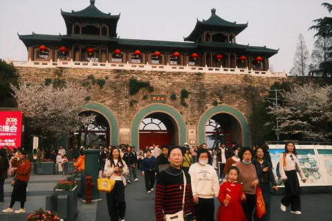 A crowd of people leave the gate to the Xuanwu Lake in Nanjing. At the front of the crowd, a family, the young daughter dressed in red, look towards the camera.