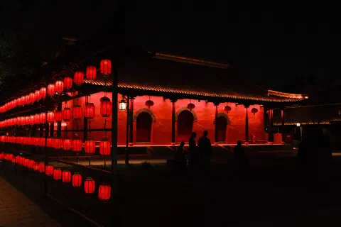 a temple lit up at night, the red paint and red lanterns dominate the image