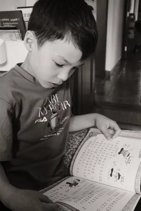 A black and white photo of a boy reading a Chinese book.