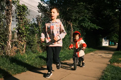 Two boys head along a footpath, the elder one running, the younger on a balance bike.