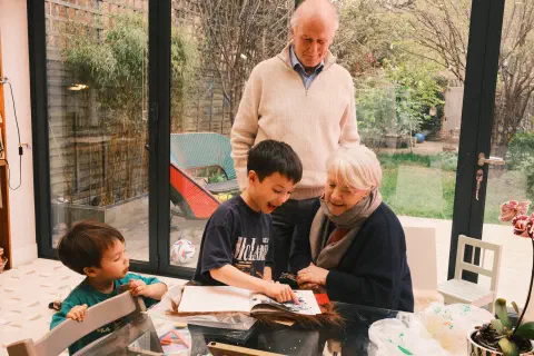 A family gathers round a table looking at something in a book.