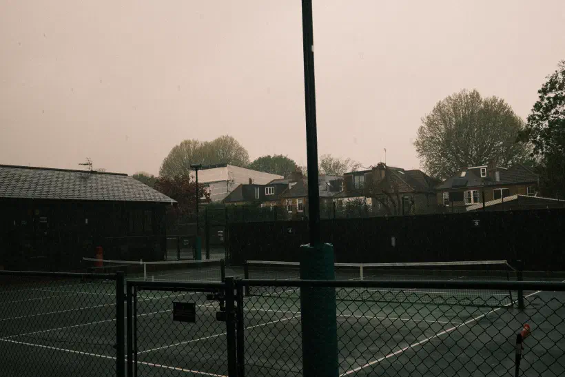 a photo looking out over a wet tennis court, the dark sky hiding the fact that this is mid morning