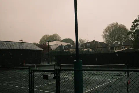 a photo looking out over a wet tennis court, the dark sky hiding the fact that this is mid morning