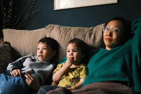 a family sits on a sofa looking at a TV thatt is off camera