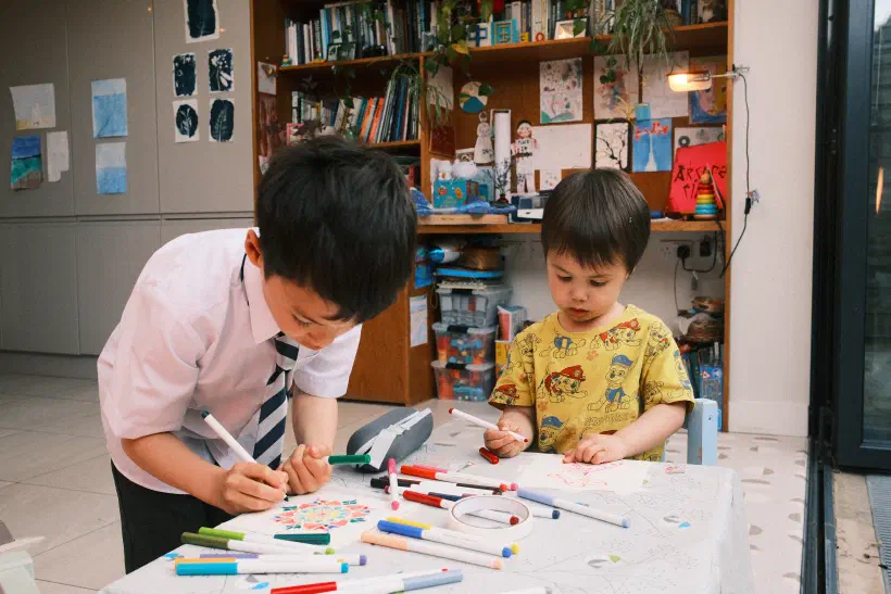 two boys hunched over a small table making greetings cards, the table covered in felt pens